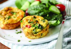 two small muffins on a white plate next to some vegetables and a fork