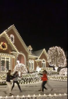 two people walking in front of a house covered in christmas lights