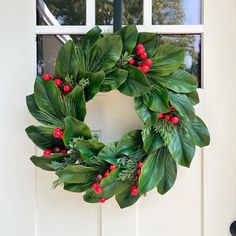 a wreath with holly and red berries hanging from the front door, next to a window