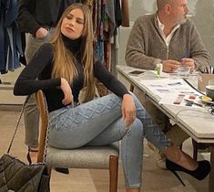 a woman sitting in a chair at a table with two men standing behind her and holding a handbag