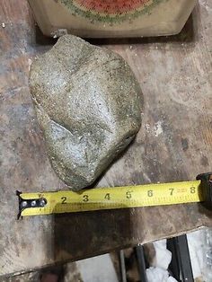 a large rock sitting on top of a wooden table next to a measuring tape and a clock