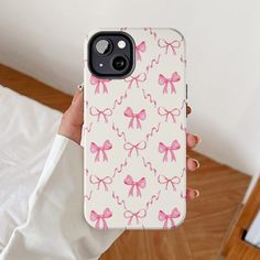 a woman holding up her phone case with pink bows on it, in front of a bed