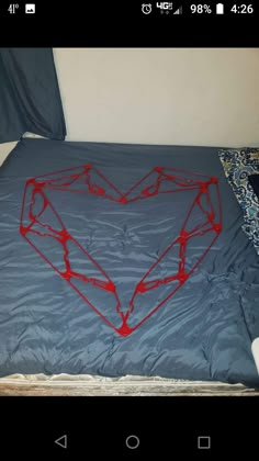 a bed with a heart made out of red string on it's side and blue sheets