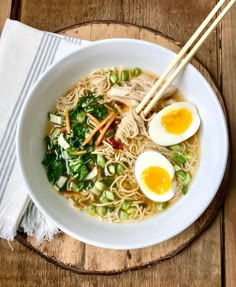 a white bowl filled with ramen and eggs on top of a wooden table next to chopsticks