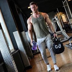 a man with headphones and no shirt is holding a gym bag while walking through the gym