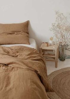 a bed with brown sheets and pillows in a white room next to a small table