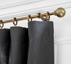 two black curtains are hanging on a rod in front of a white door with gold hardware