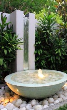 a bowl shaped fountain in the middle of a garden with rocks and plants around it