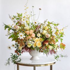 a white vase filled with lots of flowers on top of a marble topped side table