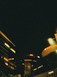 a traffic light in the middle of a city at night with buildings lit up behind it