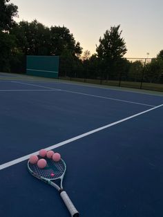 a tennis racket and four balls on the court at sunset or sunrise, with trees in the background