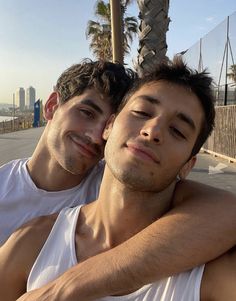 two young men sitting next to each other in front of palm trees and the ocean