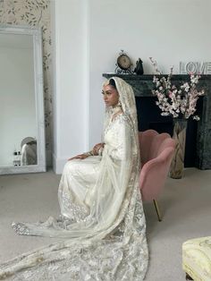 a woman in a white wedding dress sitting on a pink chair next to a fireplace