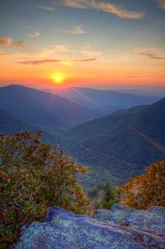 the sun is setting in the mountains with rocks and trees on it's sides