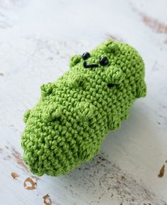 a green crocheted stuffed animal sitting on top of a white surface with black eyes