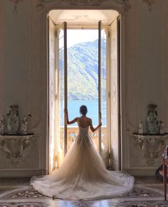 a woman in a wedding dress is looking out an open door at the lake and mountains