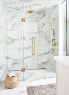 a white marble bathroom with gold fixtures and glass shower doors, including the door handle