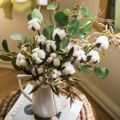 a white pitcher filled with cotton sitting on top of a table next to a plant