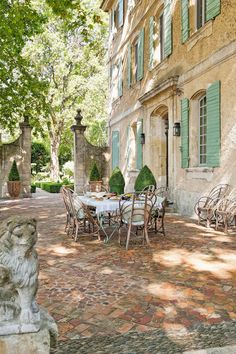 an outdoor table and chairs in front of a building with green shutters on the windows