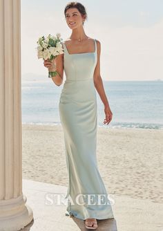 a woman standing on the beach in a long dress holding a bouquet of white flowers