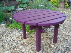 a purple table sitting on top of a pile of wood shaving next to a garden