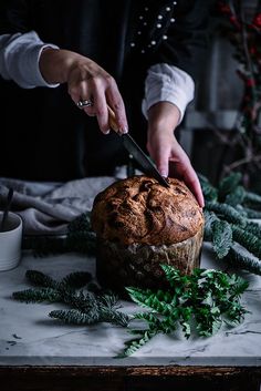 a person cutting into a loaf of bread on top of a table with greenery