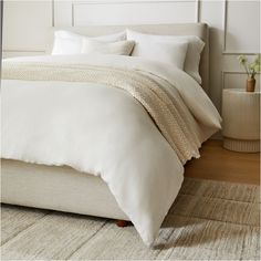 a bed with white linens and pillows in a small room next to a plant