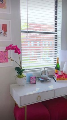 a white desk with pink stools in front of it and pictures on the wall