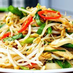 a white plate topped with noodles and veggies on top of a wooden table