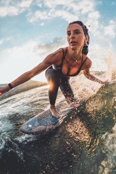 a woman riding a surfboard on top of a wave in the ocean at sunset