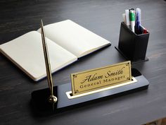 a desk with an open book, pen and pencil holder on it that says alarm smith general manager