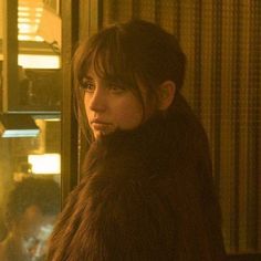 a woman standing in front of a window wearing a fur coat and looking off into the distance