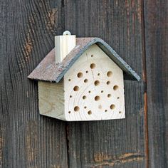 a wooden bird house with holes in it's roof hanging on a wood fence