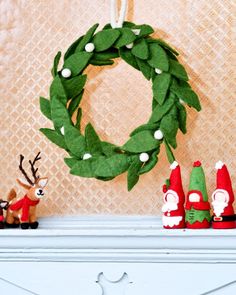 a christmas wreath is hanging on the mantle next to three gnomes and an elf figurine