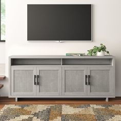 a flat screen tv mounted to the side of a wall above a gray cabinet with doors