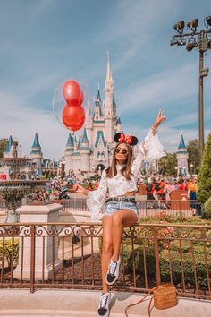 a woman sitting on top of a metal fence next to a red balloon in front of a castle