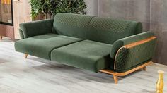 a green couch sitting on top of a hard wood floor next to a potted plant