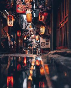 a narrow alley with lanterns hanging from it's ceiling and lights reflecting in the water