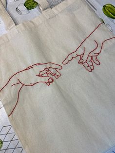 two hands touching each other with red thread on the canvas tote bag that has been embroidered onto it