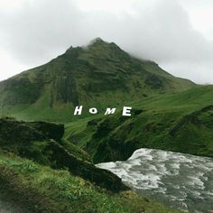 the word home is written in front of a green mountain with water flowing below it