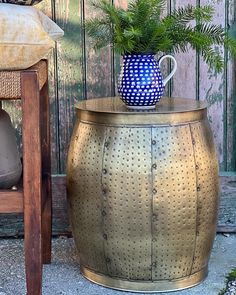 a potted plant sitting on top of a metal barrel next to a wooden chair