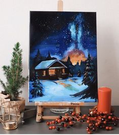 a painting on an easel with christmas decorations around it and a candle in the foreground