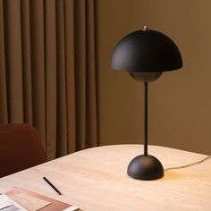 a black lamp sitting on top of a wooden table next to a book and pen