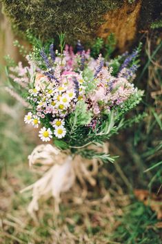 a bouquet of wildflowers and daisies tied to a mossy tree trunk