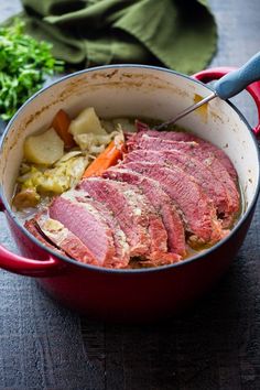 a pot filled with meat and vegetables on top of a wooden table next to a green cloth