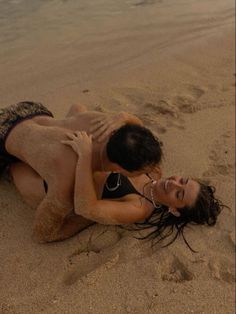 two people are laying on the beach in swimsuits and one is holding onto another person's back