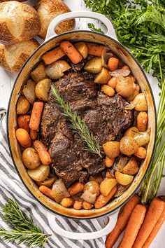 pot roast with carrots, potatoes and parsley on a striped towel next to croissants