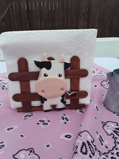 a small cow is standing in front of a wooden fence on a pink table cloth