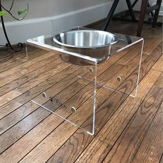 a dog bowl is sitting on top of a clear acrylic stand in the middle of a wood floor