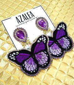 purple and black butterfly earrings with crystal accents on a gold background next to a card